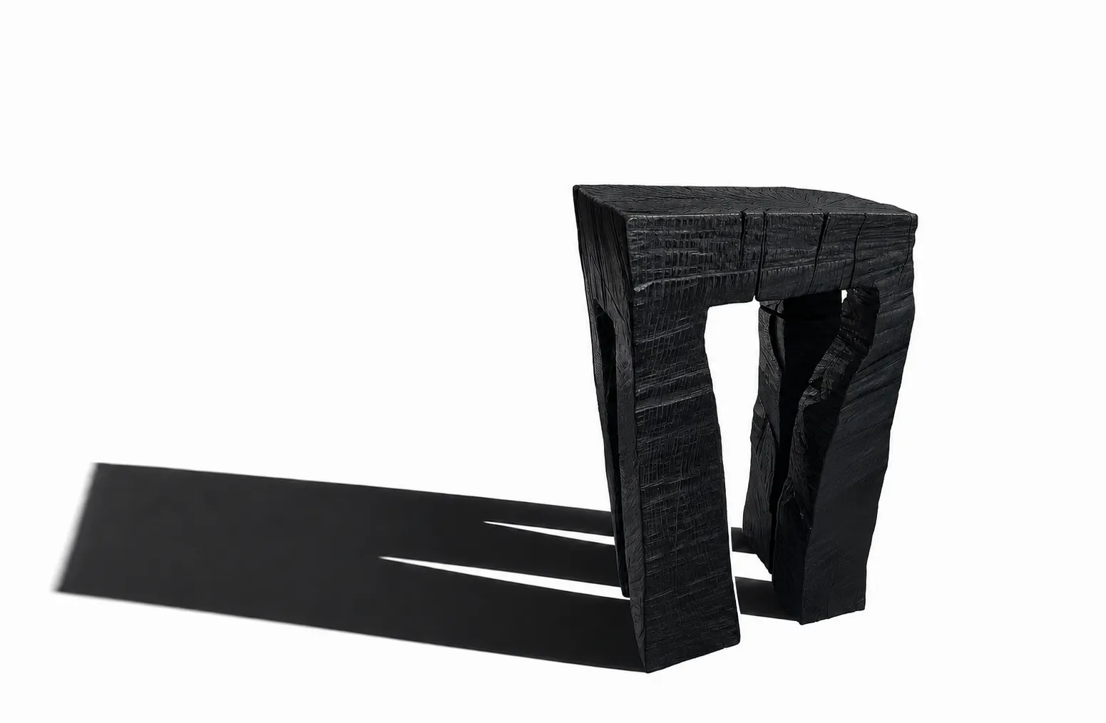 Black oak stool with a roughly hewn surface on a white ground, casting a long shadow
