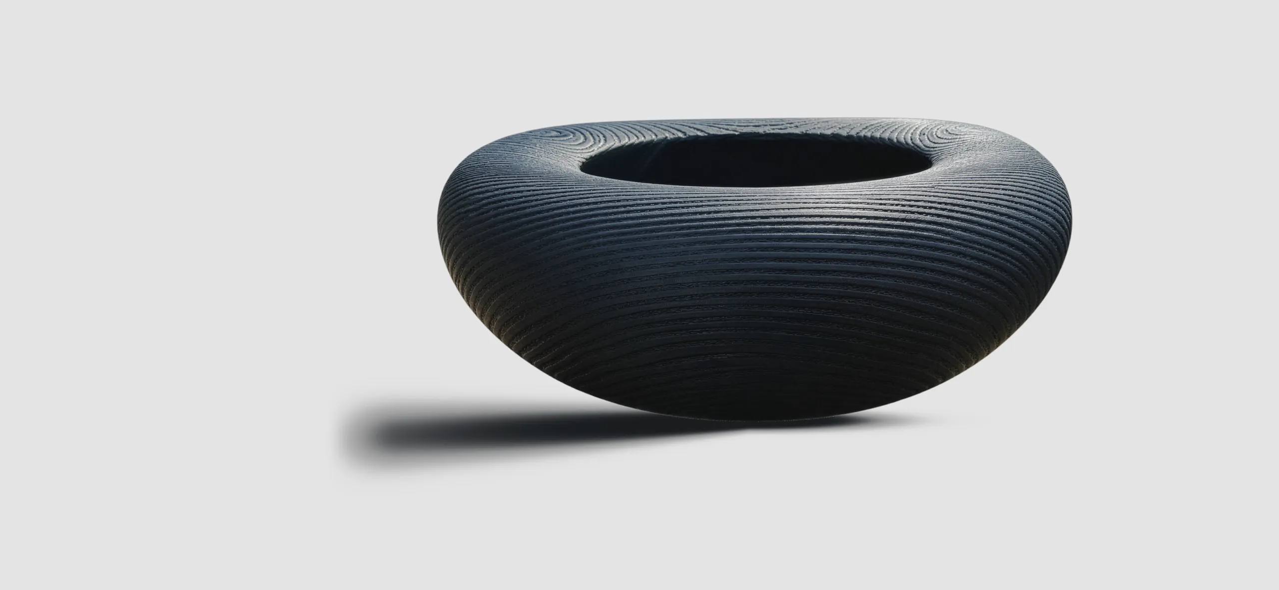 Dark matt ash bowl with a broad rim and ridged wood grain on a light ground, casting a shadow to the left